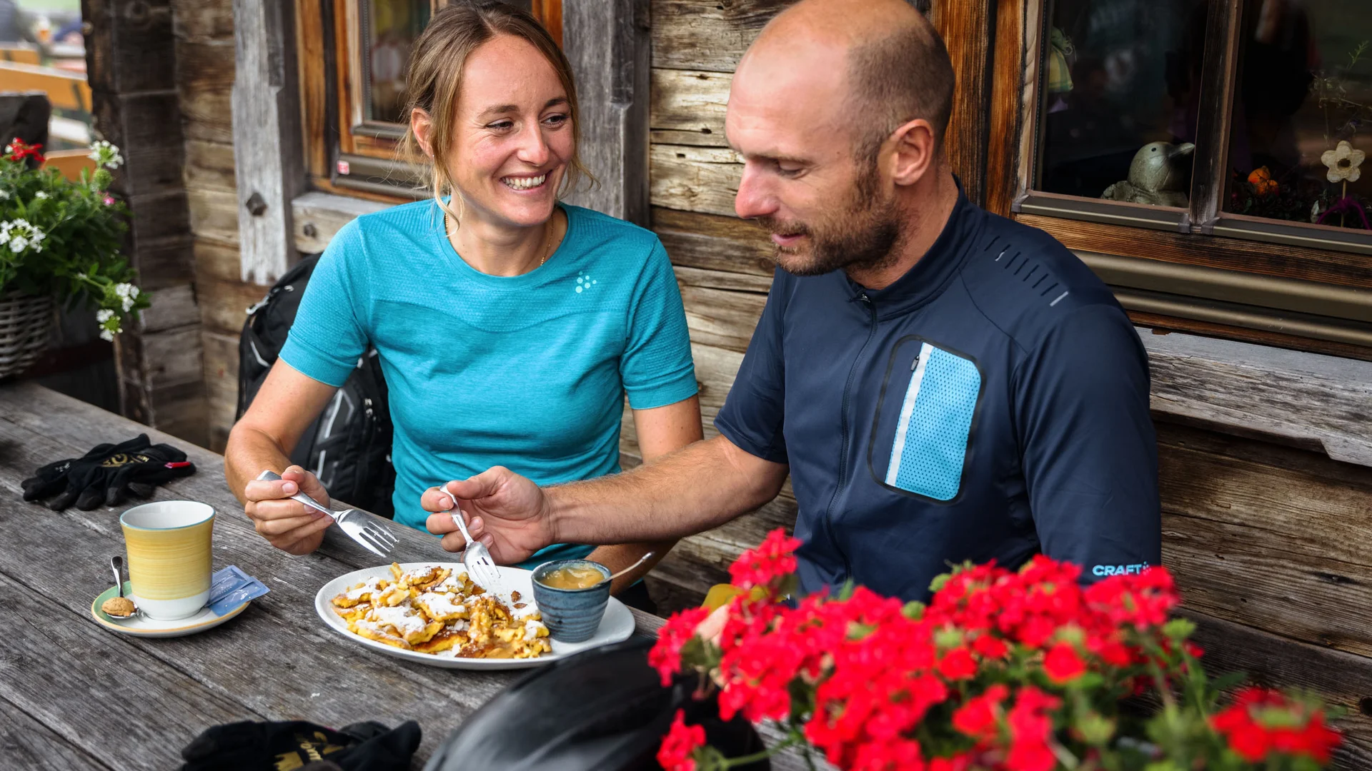 Paar isst Kuchen und trinkt Kaffee auf Holztisch vor Holzhütte