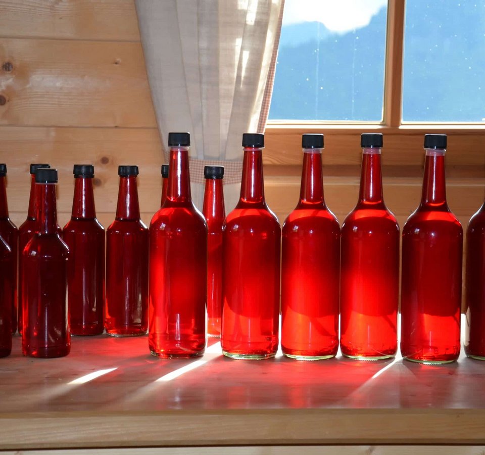 Row of red bottles on wooden table in front of window with curtain
