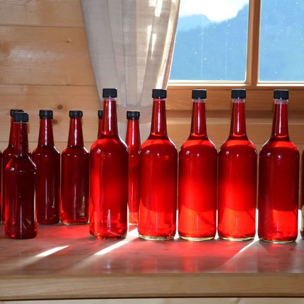 Row of red bottles on wooden table in front of window with curtain