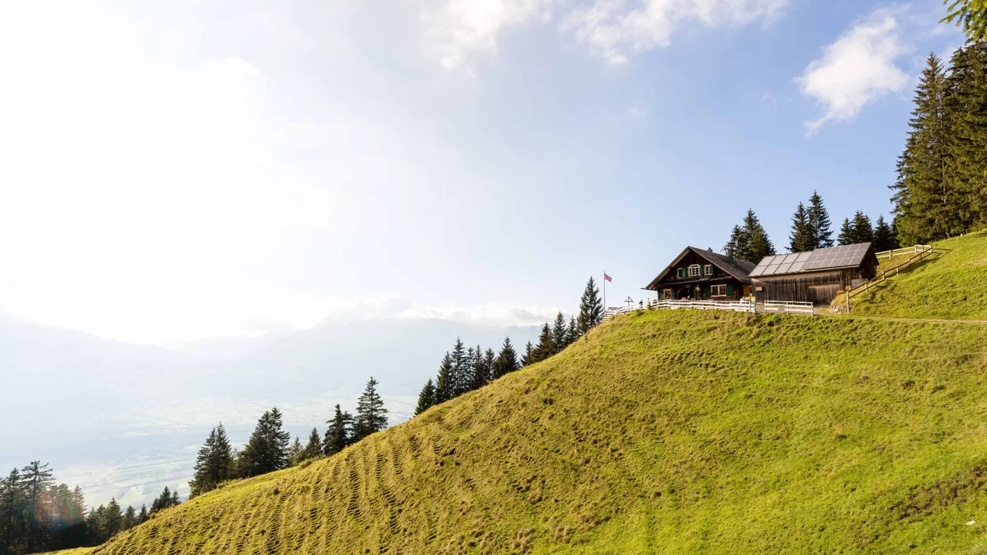 Holzhaus auf grünem Hügel mit Wald und blauem Himmel