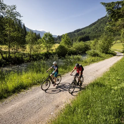 Twee fietsers rijden op een bospad naast een rivier in de bergen