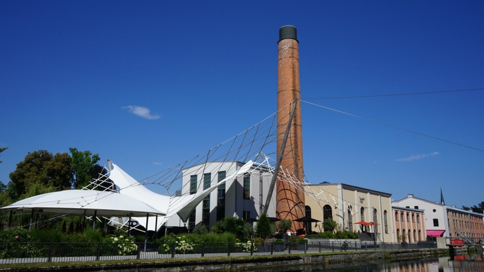 Industrial building with chimney and tent structure by the water