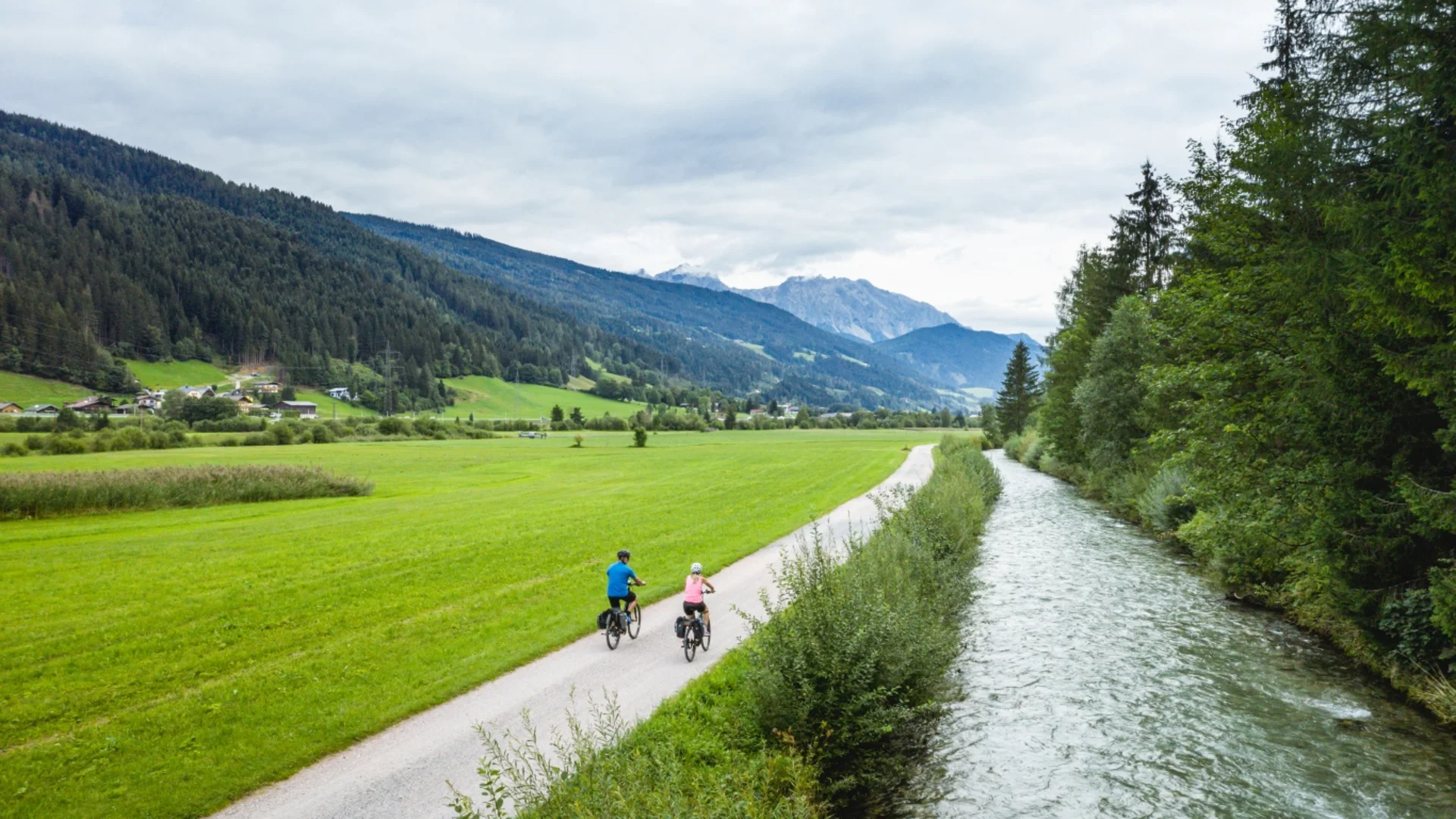 Zwei Radfahrer auf Weg neben Fluss in grüner Berglandschaft