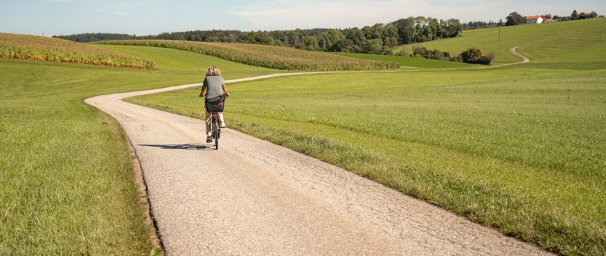 3 Gründe fürs Herbst-Radln in Inn-Salzach © Tourismusverein Inn-Salzach Frau radelt auf Landstraße durch grüne Felder unter blauem Himmel