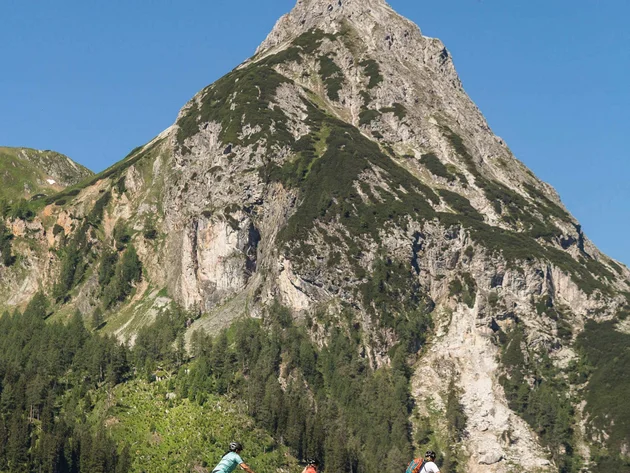 Drei Radfahrer fahren vor einem großen Berg im Sommer