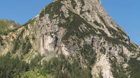 Drei Radfahrer fahren vor einem großen Berg im Sommer