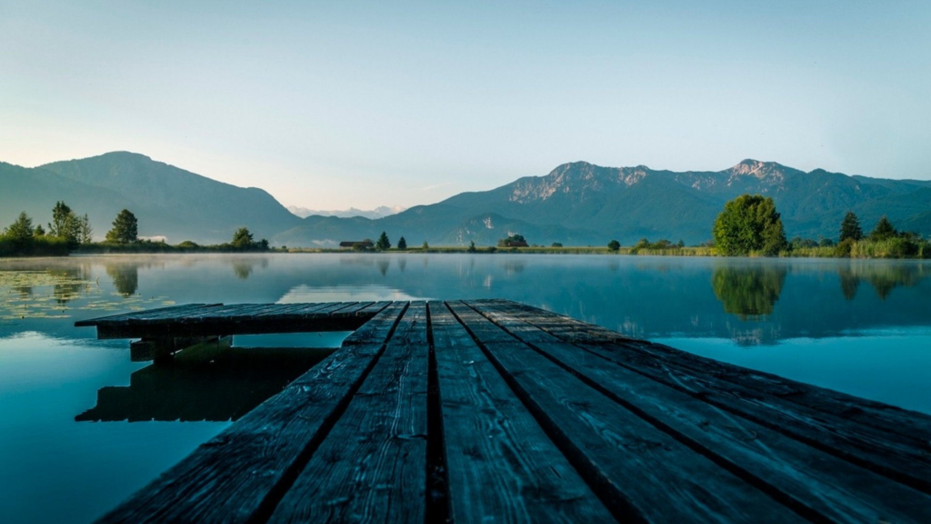 Wooden dock over calm lake with mountains and trees in the background
