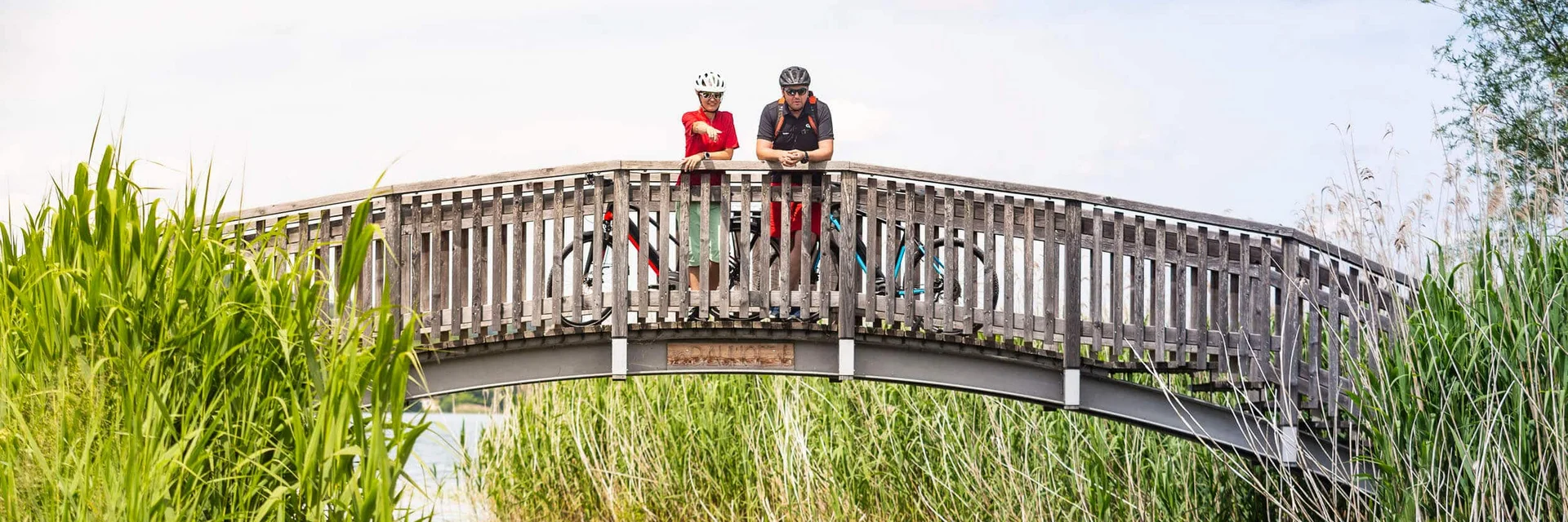 Twee fietsers op een houten brug over een rivier omgeven door riet