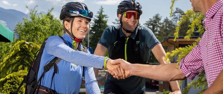 Two cyclists greeting and shaking hands with a man outdoors