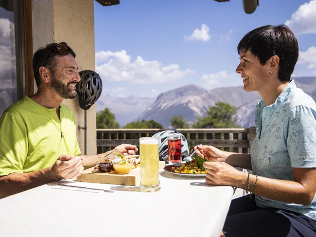 Drei Länder, du und dein Rad: Den Reschensee grenzüberschreitend entdecken © Heiko Mandl Zwei Personen essen auf Terrasse mit Bergblick bei sonnigem Wetter