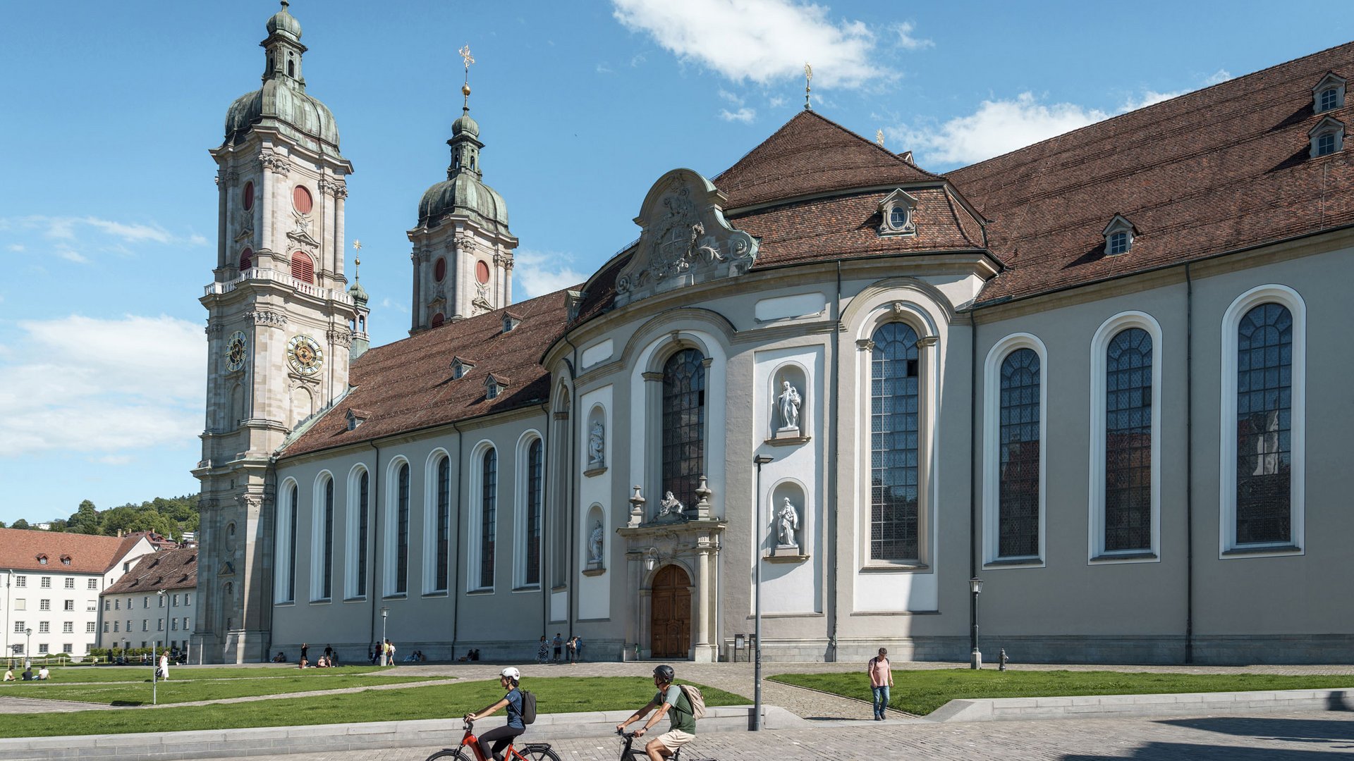 Church building with towers and cyclists in front on a sunny day
