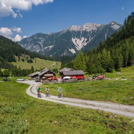 Cyclists on mountain path near huts with mountains in background