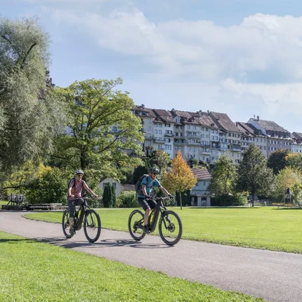 Twee personen fietsen op een pad in een park op een zonnige dag