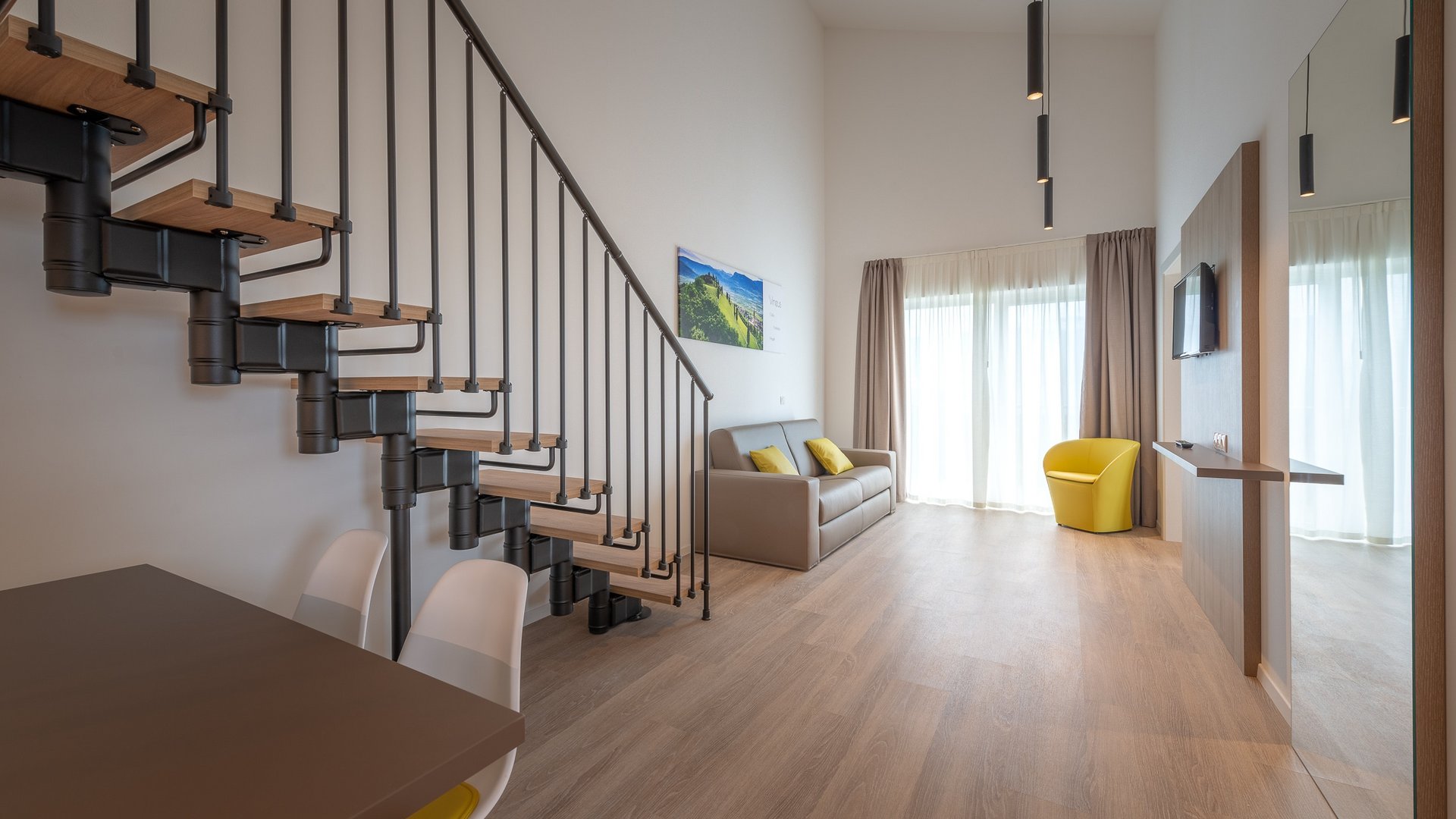 Modern living room with staircase, sofa and yellow armchair by large window