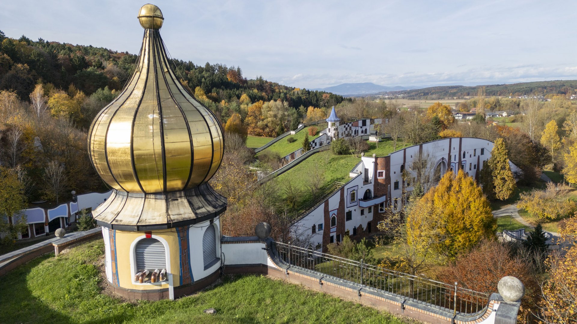 Golden onion dome and colorful building in hilly landscape with autumn trees