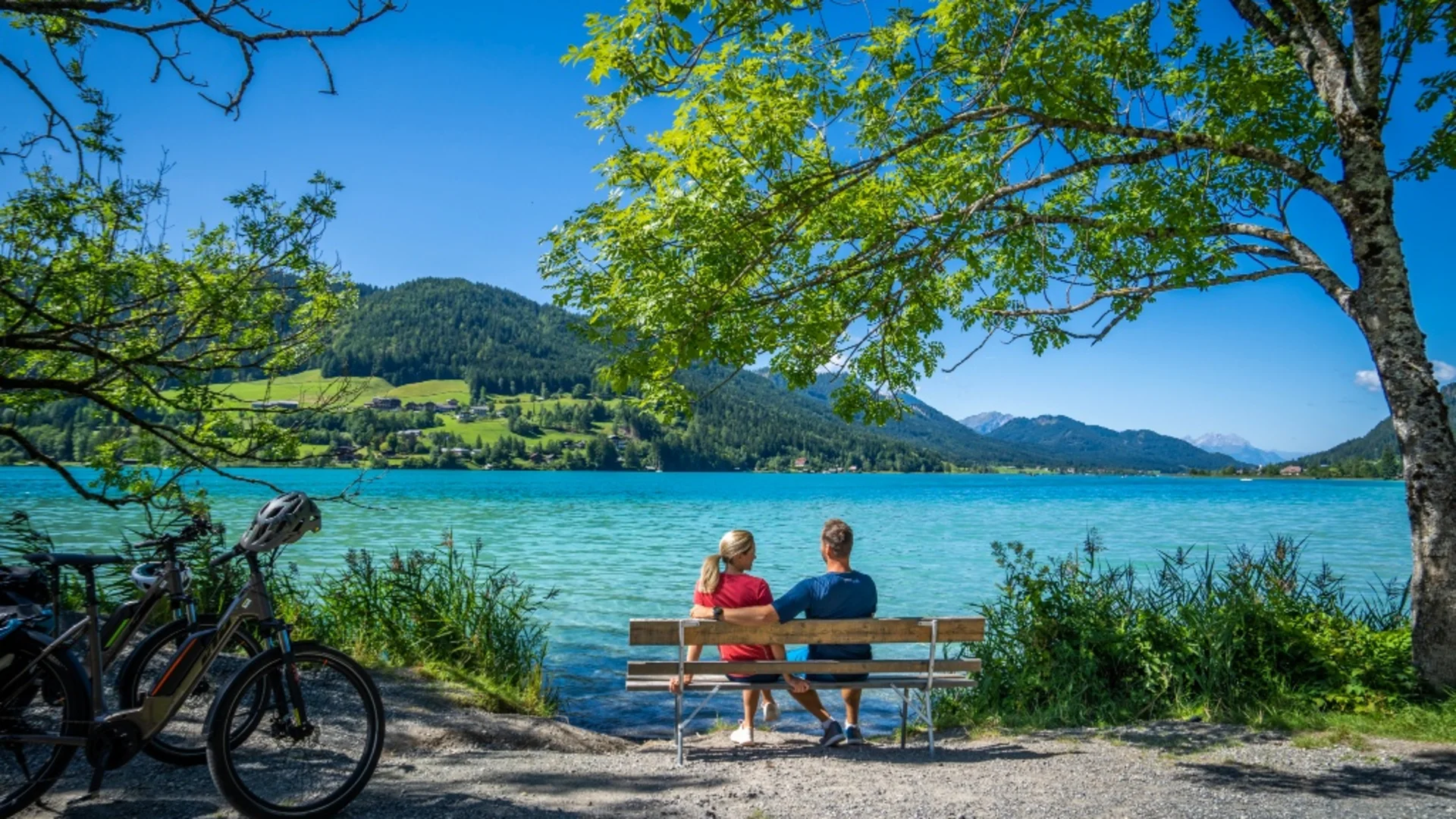 Stel zit op bankje bij meer met uitzicht op bergen bij zonnig weer