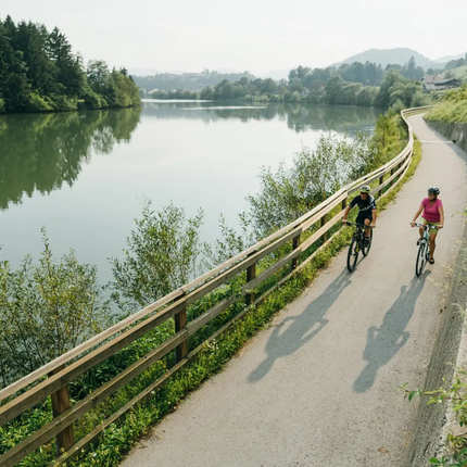 Two cyclists riding on a path beside a calm river in green countryside
