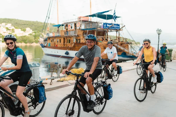 Kultur, Natur und Meer auf Rad- & Schiffsreisen © Kleomenis Koufaliotis Gruppe von Radfahrern mit Helmen entlang eines Kai mit einem Holzboot im Hintergrund