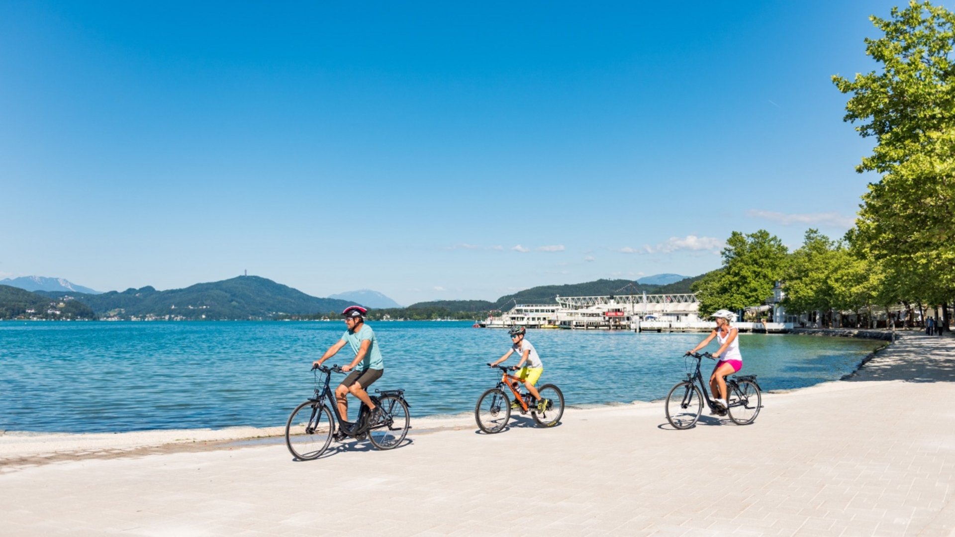 Family cycling along lakeside with mountains in the background