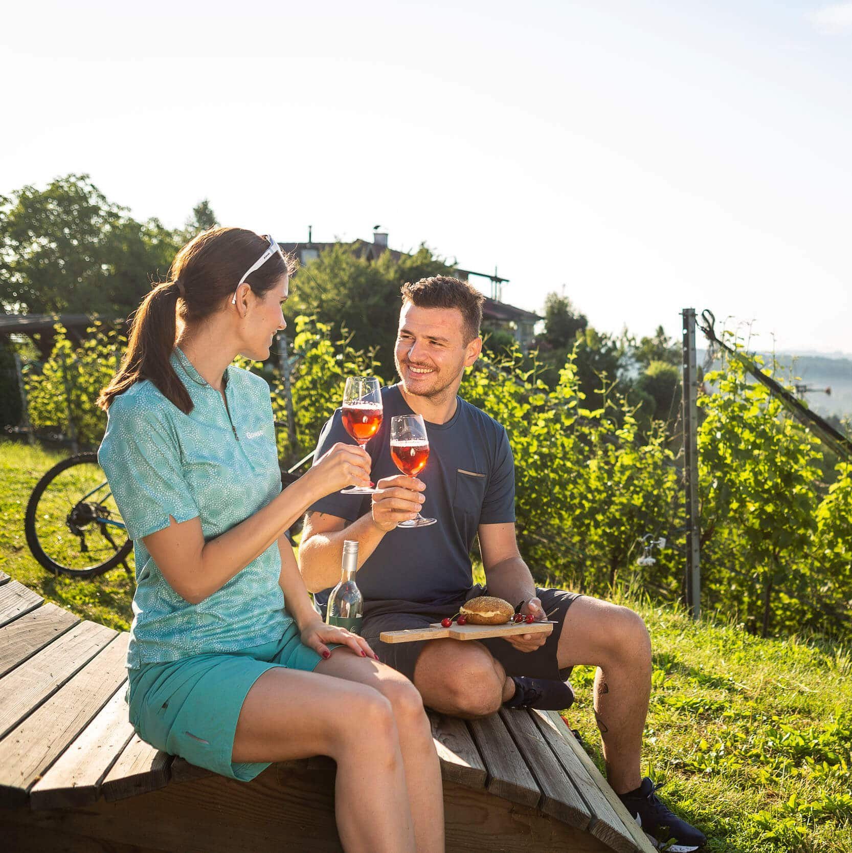 Paar trinkt Wein und genießt Snack im Weinberg bei Sonnenschein