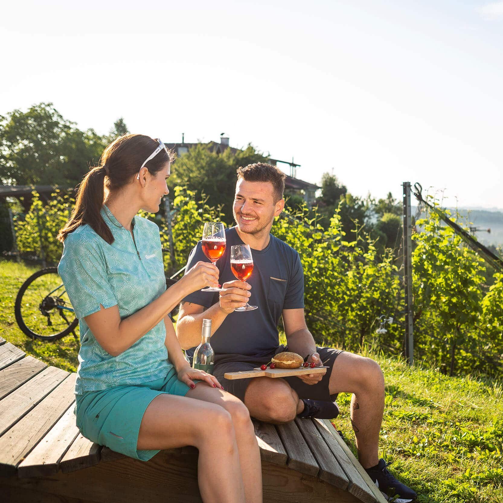Paar trinkt Wein und genießt Snack im Weinberg bei Sonnenschein