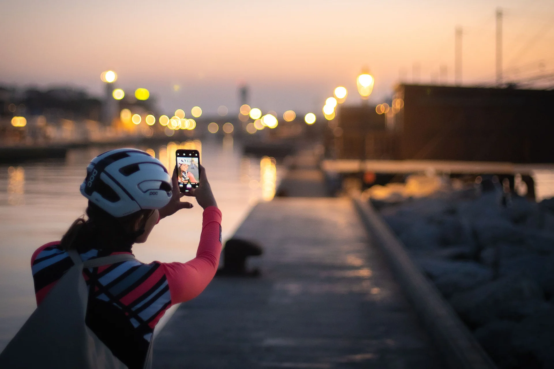 Person mit Helm macht Foto am Wasser bei Sonnenuntergang