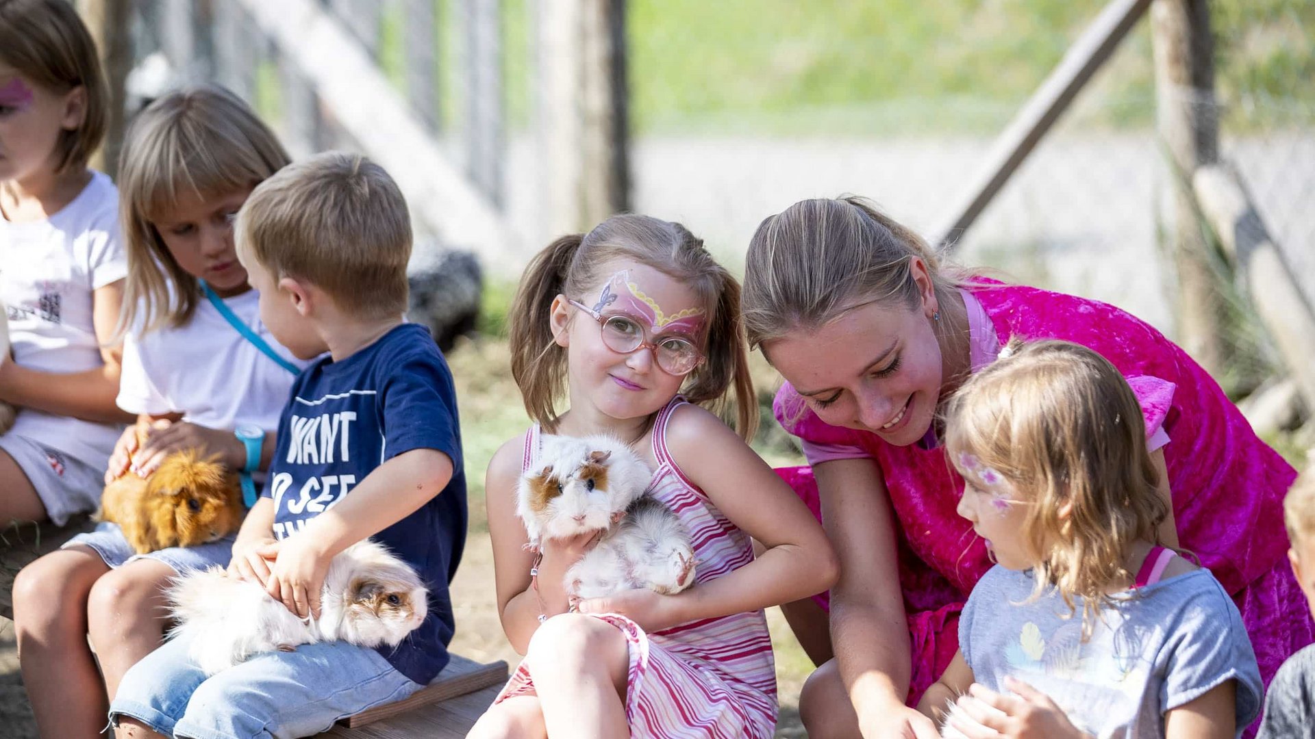Children with face paint holding guinea pigs outdoors
