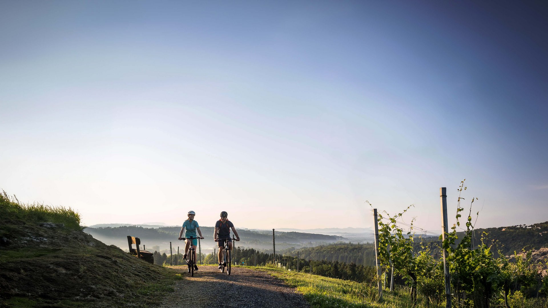 Two cyclists riding on a path in a hilly landscape under clear sky