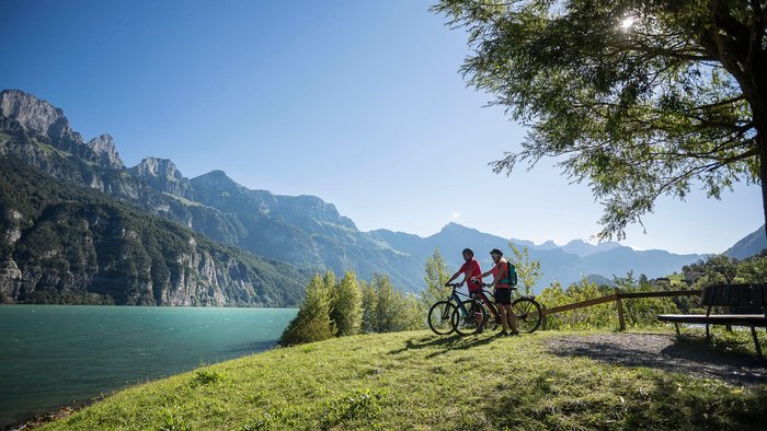 Zwei Radfahrer genießen den Blick auf Bergsee und Berge bei sonnigem Wetter