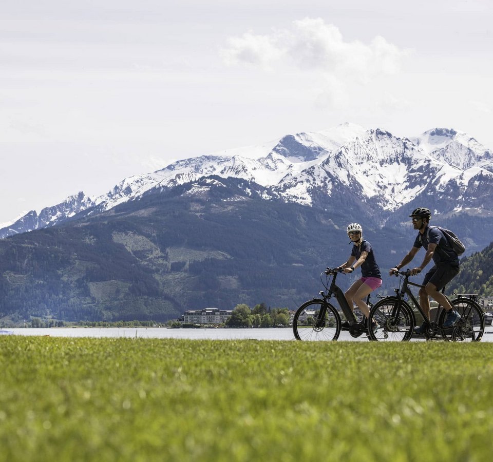 Zwei Radfahrer vor schneebedeckten Bergen und einem See