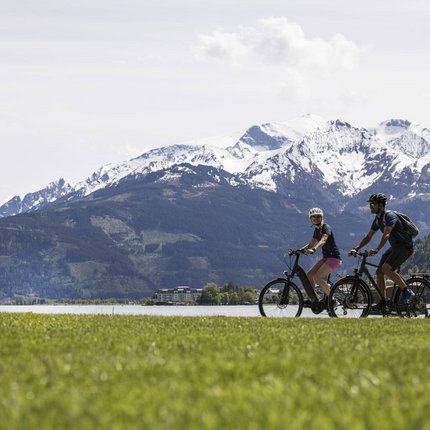Zwei Radfahrer vor schneebedeckten Bergen und einem See