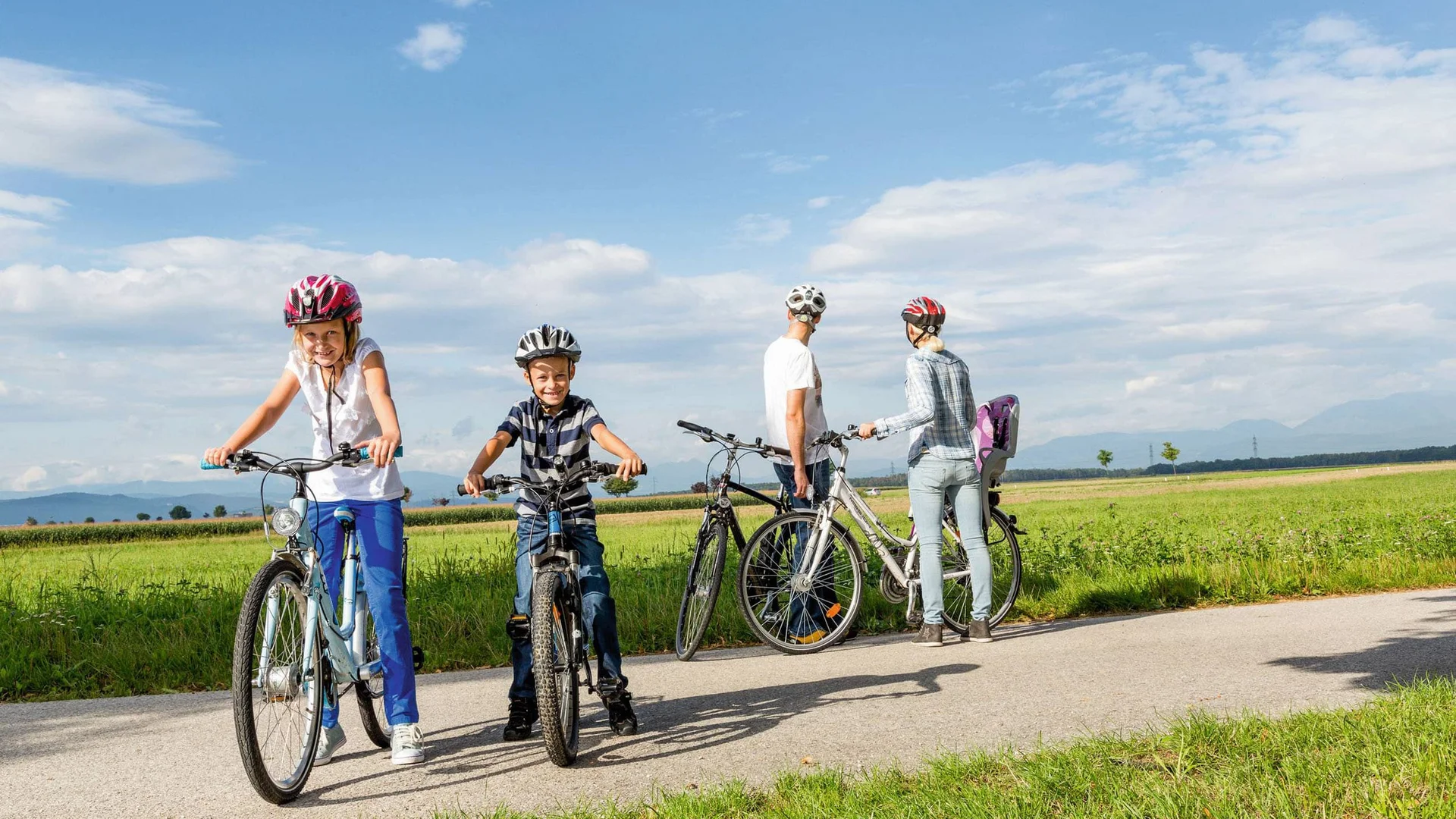 Familie mit Kindern fährt Fahrrad auf Landstraße bei schönem Wetter