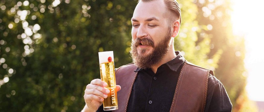Bearded man holding a glass of beer outdoors in sunlight