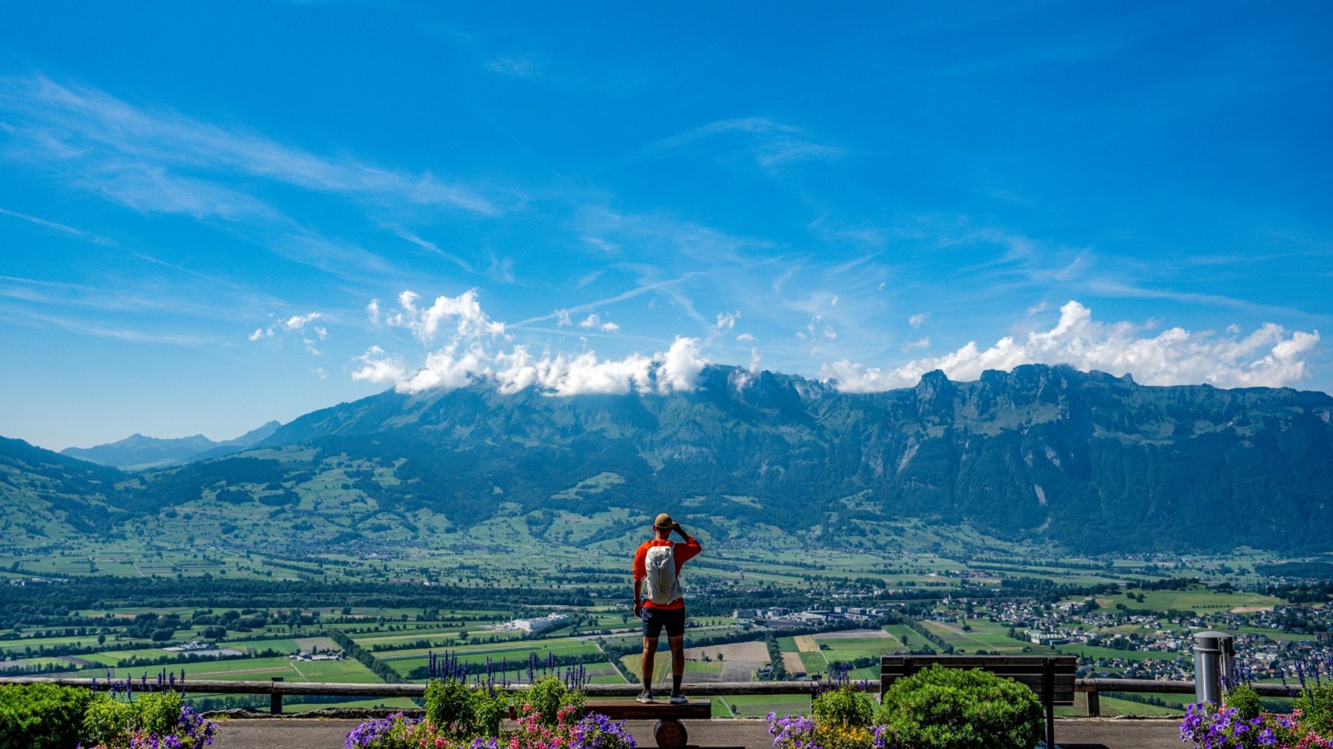Person looks at valley and mountains under clear sky