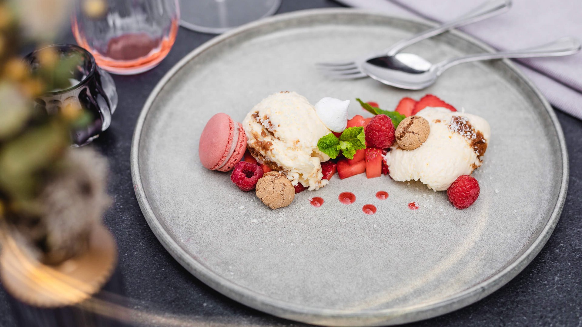 Dessert with macaron, ice cream, berries, and mint on a gray plate