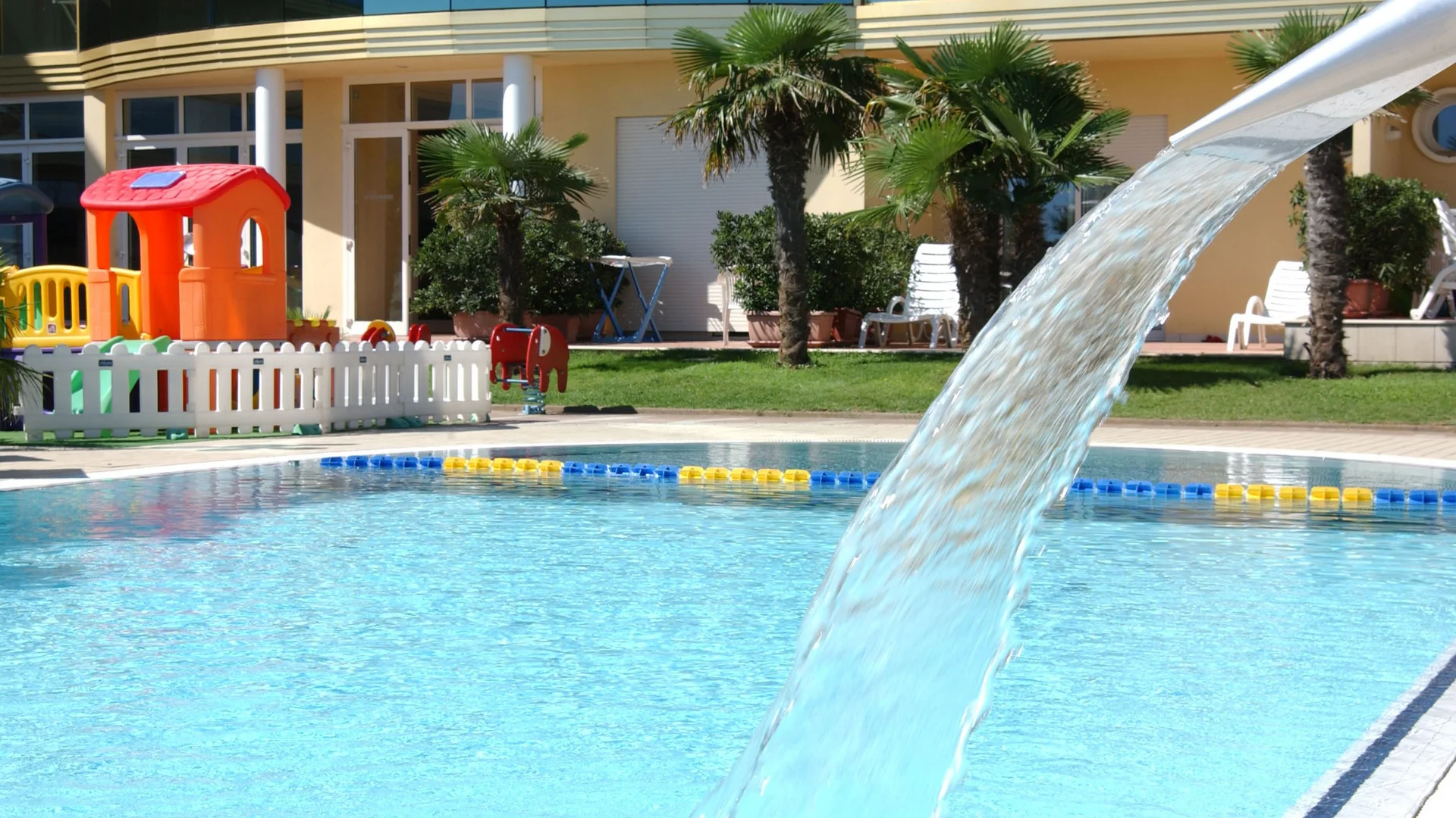Waterfall in pool with playground and palm trees in background