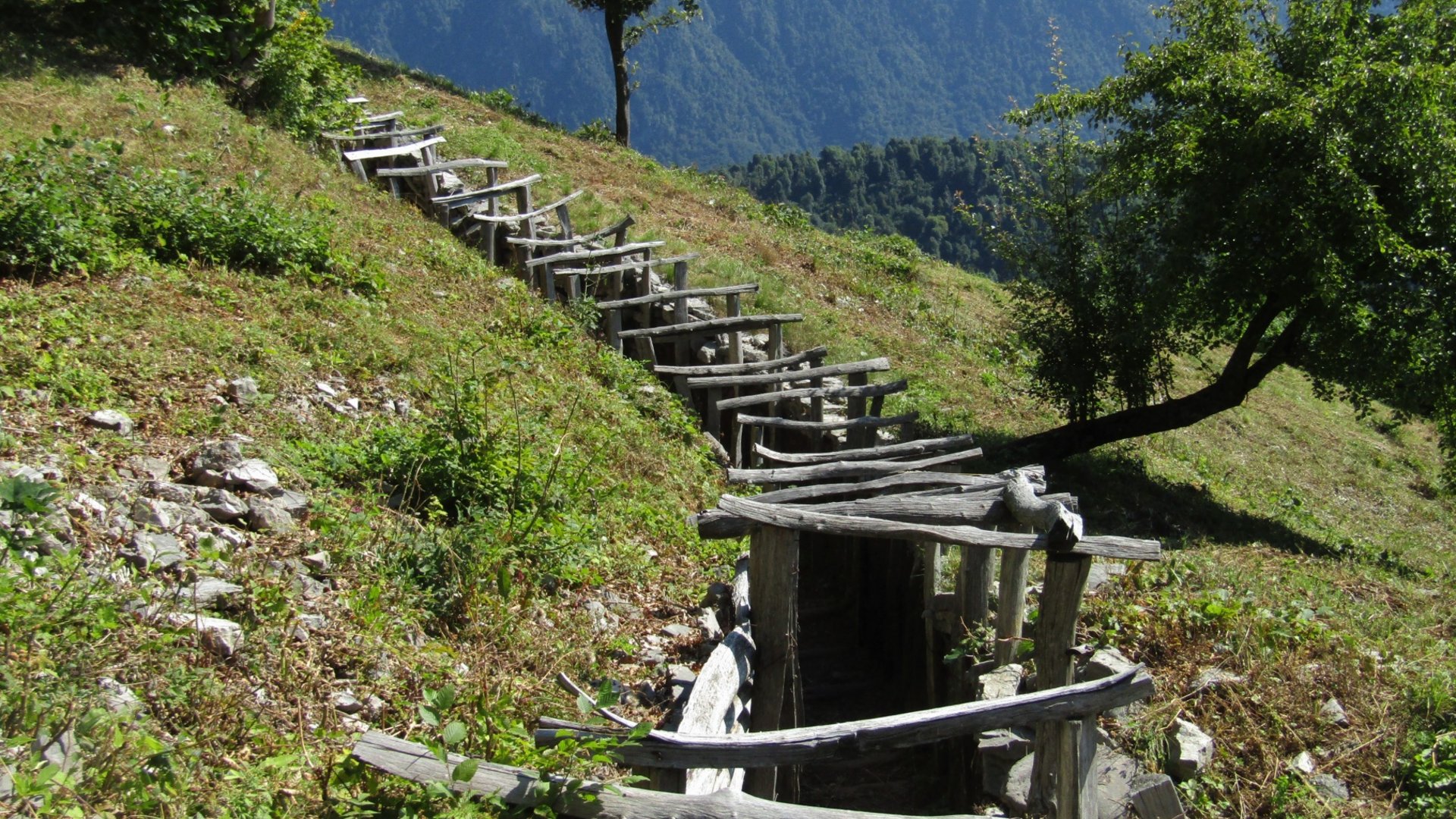 Old wooden structure on a grassy hillside with mountains in the background