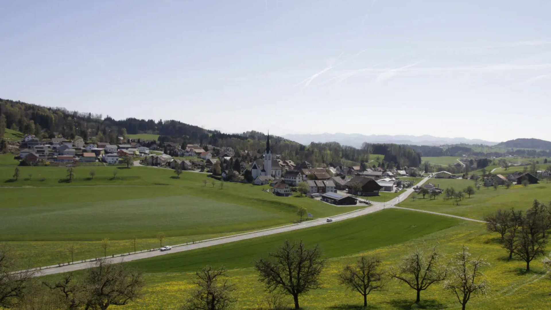 Village with church and green fields under clear blue sky