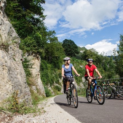 Two cyclists on mountain path with people resting on bench nearby