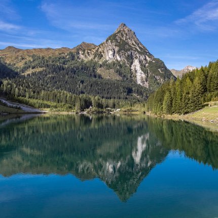 Pointed mountain peak with forest and lake, clear reflection in water