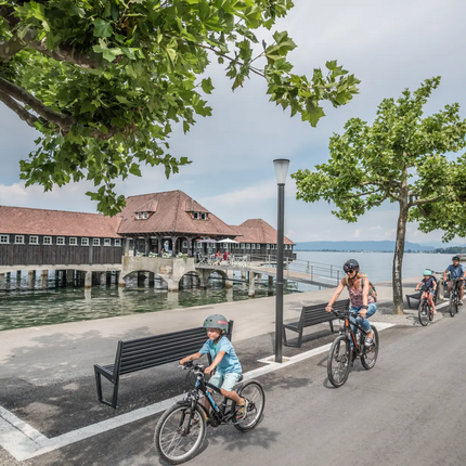 Family cycling along lakeside path near a historic wooden pier