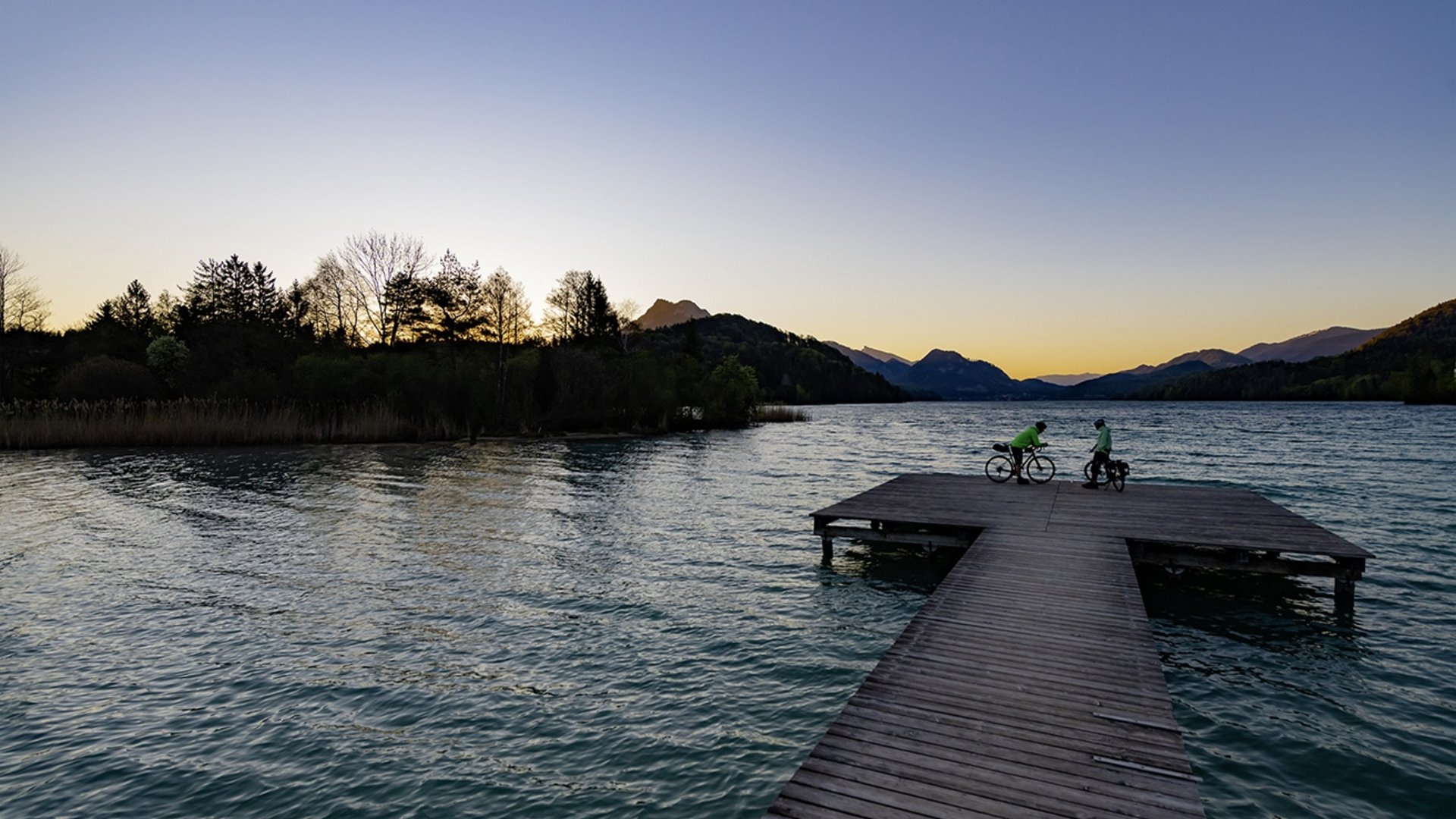 Schöffel © Zooom.at Two cyclists on a pier over a lake at sunset