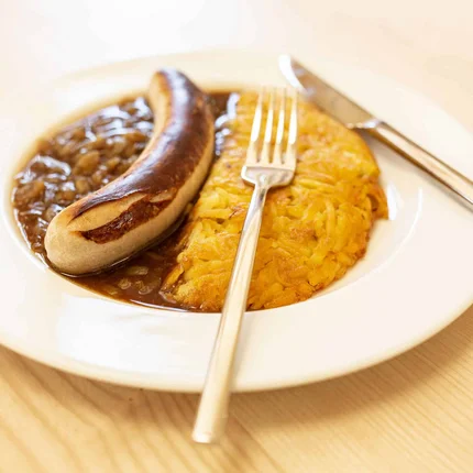 Gebraden worst met uienjus en aardappelpannenkoek op wit bord