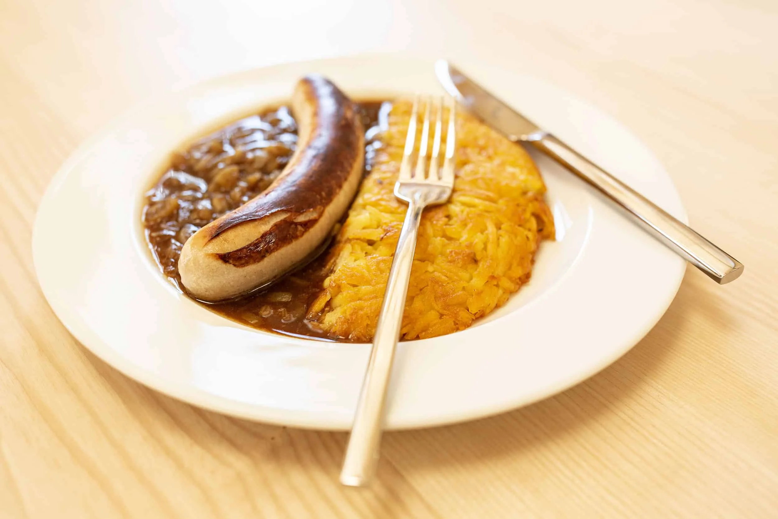 Gebraden worst met uienjus en aardappelpannenkoek op wit bord