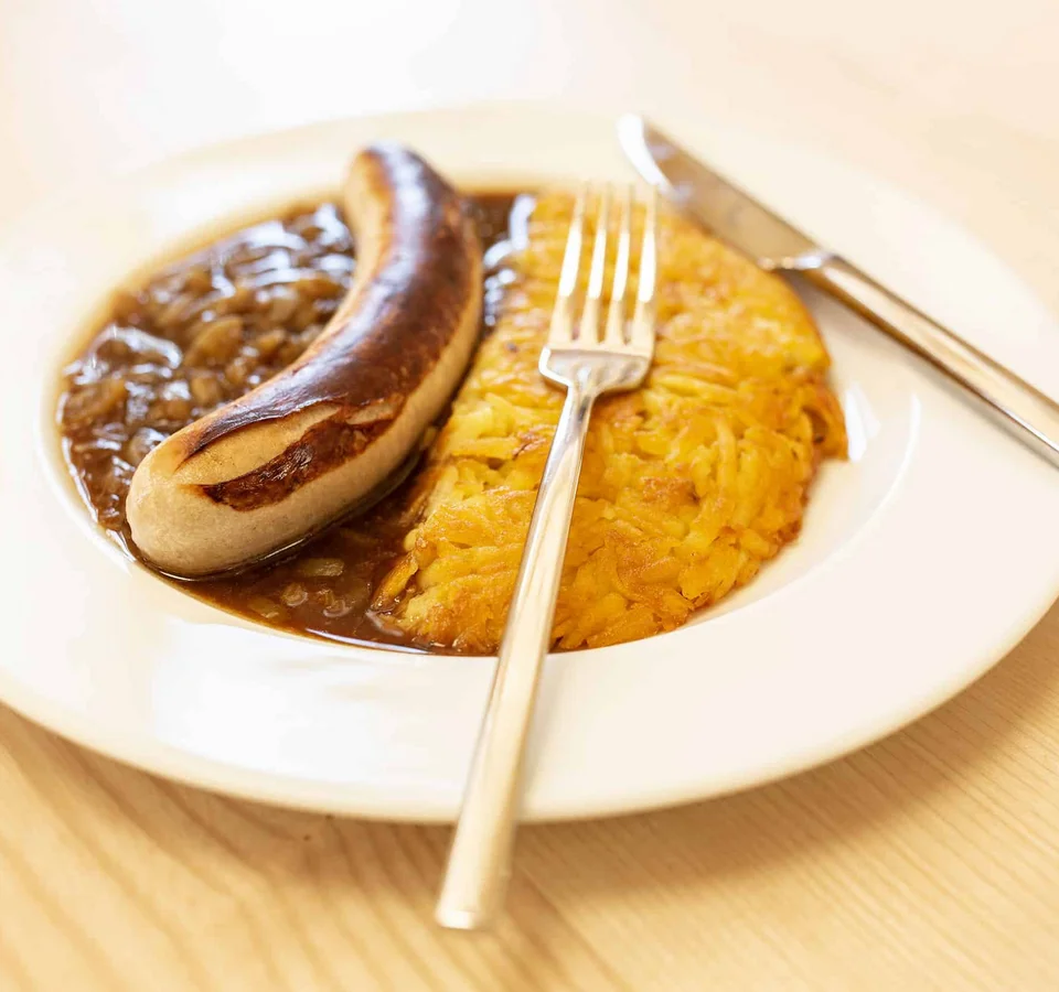 Gebraden worst met uienjus en aardappelpannenkoek op wit bord