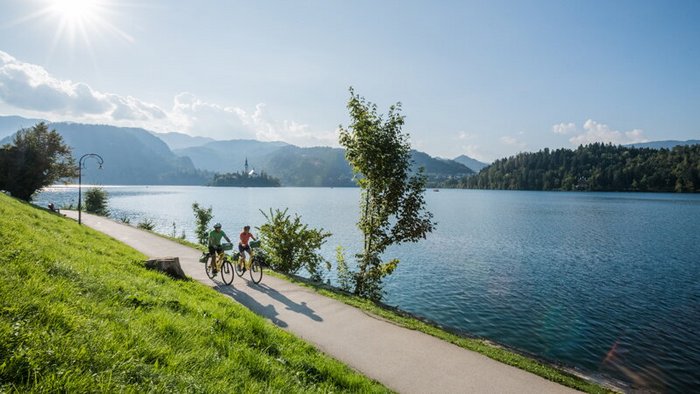 Two cyclists riding by a lake with mountains in the background