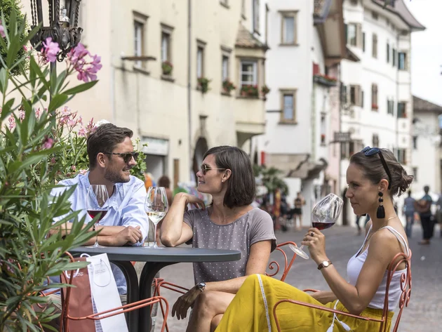 Kulinarisch unterwegs in Tramin © TV Kaltern am See - Helmuth Rier Drei Personen sitzen draußen in einem Straßencafé und trinken Wein