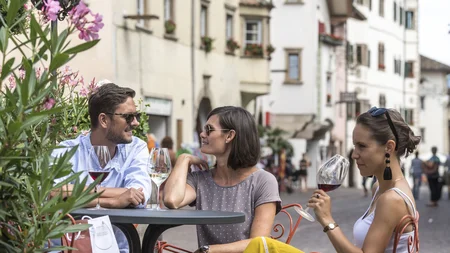 Kulinarisch unterwegs in Tramin © TV Kaltern am See - Helmuth Rier Drei Personen sitzen draußen in einem Straßencafé und trinken Wein