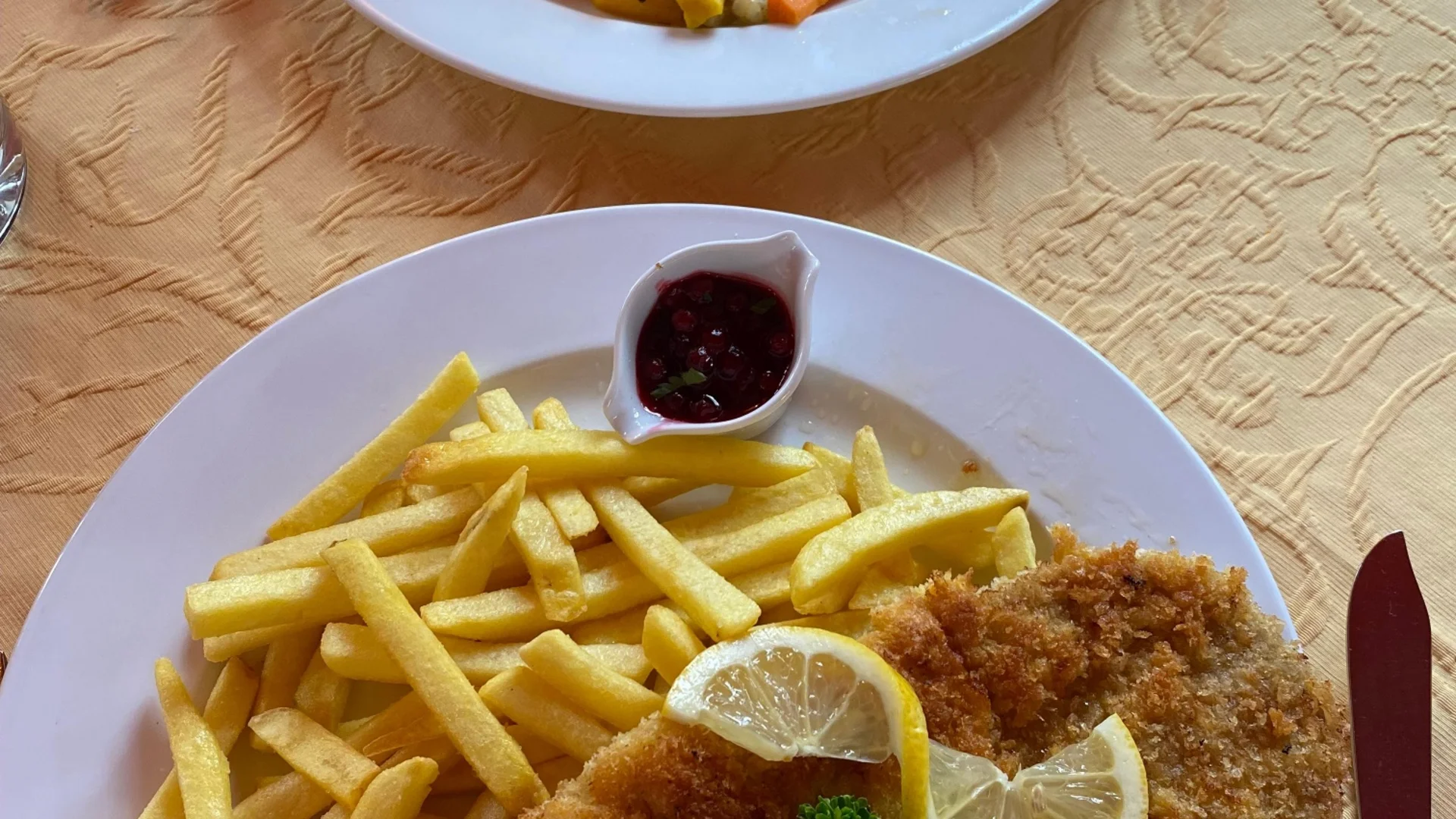 Teller mit Schnitzel, Pommes, Zitronenscheiben und Gemüse mit Kartoffeln