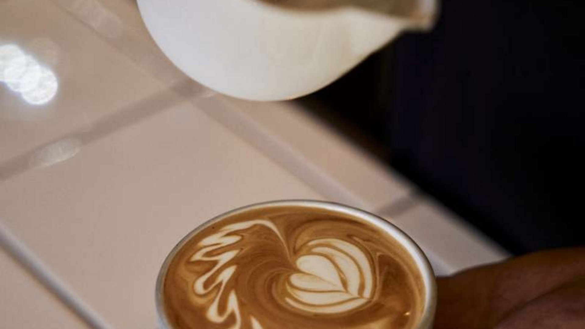Latte art in a small white cup held in a hand